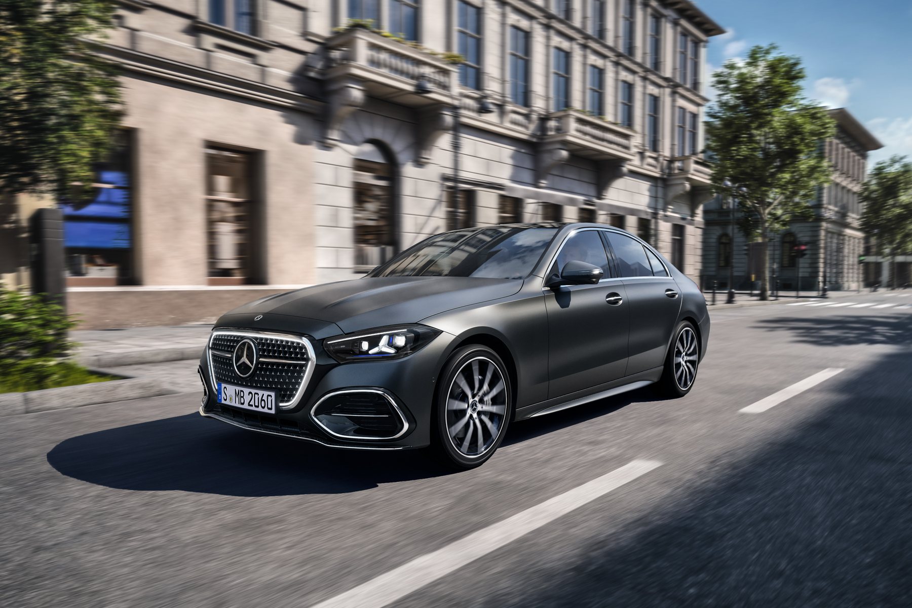 Nuevo Mercedes-Benz Clase C berlina gris circulando por una calle urbana, con la parrilla iluminada y los faros con firma lumínica de estrella